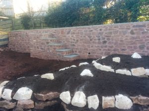 A new stone wall to replace an awkward sloping bank, capped with paving slabs, with matching steps. Fronted with a tiered, cotswold rockery filled with screened topsoil for planting.